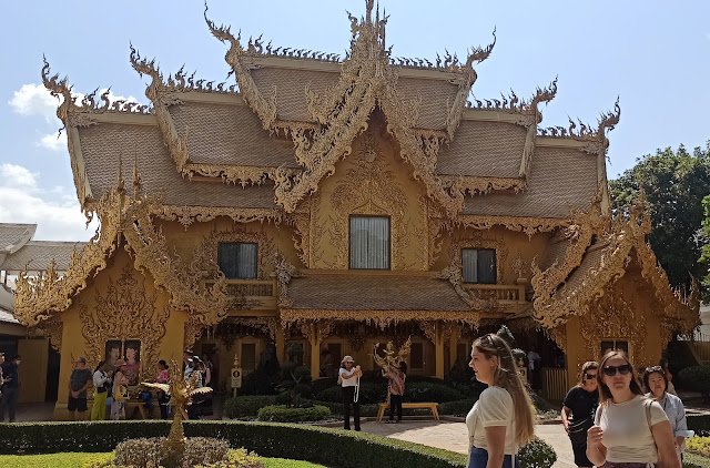 El espectacular edificio de los lavabos del Templo Blanco de Chiang Rai (Wat Rong Khun), una estructura de tres niveles completamente dorada y ricamente decorada que contrasta con la pureza del templo principal. El dorado simboliza los deseos mundanos y la atracción por lo material, en oposición al blanco que representa la pureza espiritual.