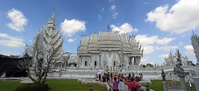 El imponente ubosot, o sala de ordenación, del Templo Blanco de Chiang Rai (Wat Rong Khun) es una estructura de un blanco impoluto que brilla con fragmentos de espejo incrustados en su exterior. Sus paredes, pintadas de blanco como símbolo de la pureza de Buda, captan la luz del sol y otorgan un brillo casi sobrenatural al edificio, convirtiéndolo en una de las imágenes más icónicas del norte de Tailandia.