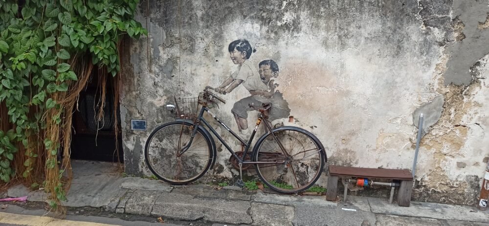 Mural 'Children on a Bicycle' de Ernest Zacharevic en la calle Armenian de Georgetown, Penang, con dos niños pintados sobre una bicicleta real. Una de las imágenes más representativas del arte callejero que Visitar GeorgeTown.